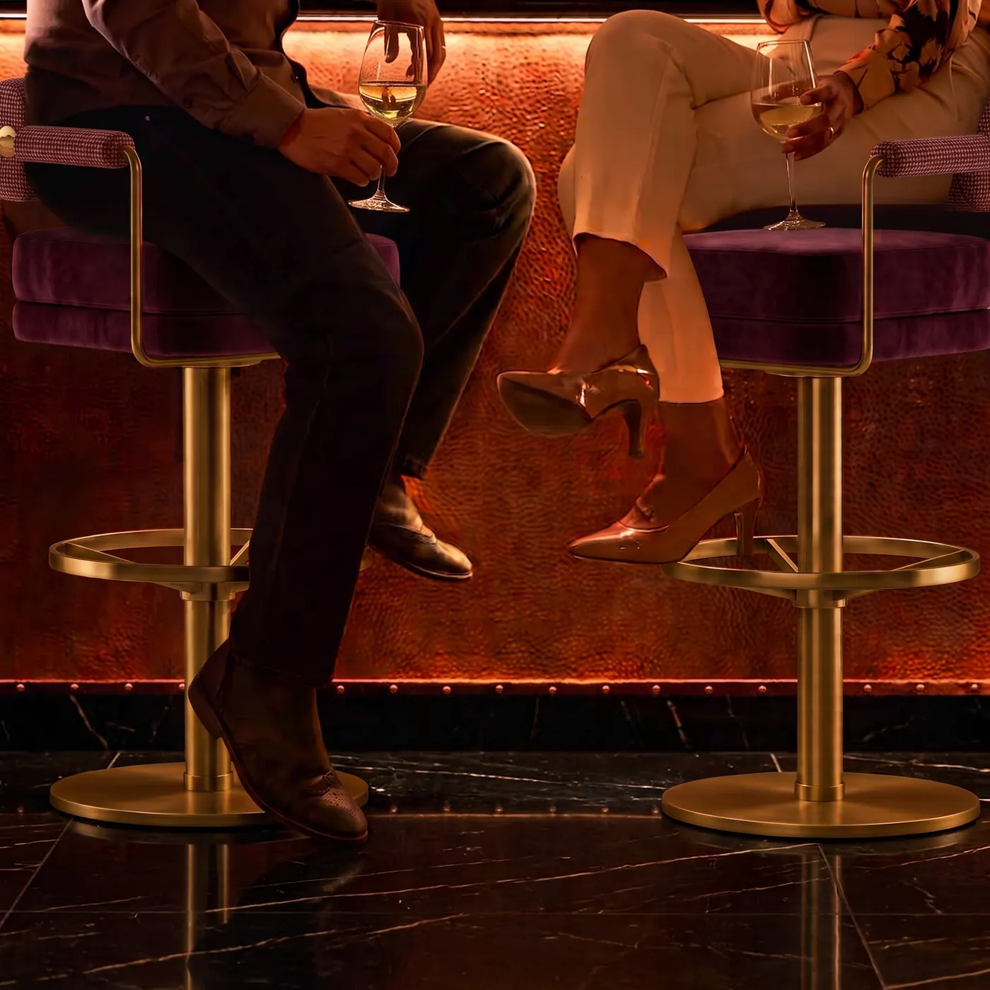 Two guests seated on brass and velvet bar stools at a copper-fronted bar