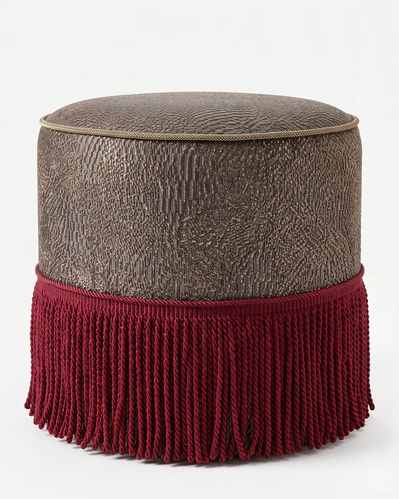 Kano Pouf pouf — round, fully upholstered pouf in a metallic pattern fabric, with a piped top edge and a deep twisted fringe skirt wra…