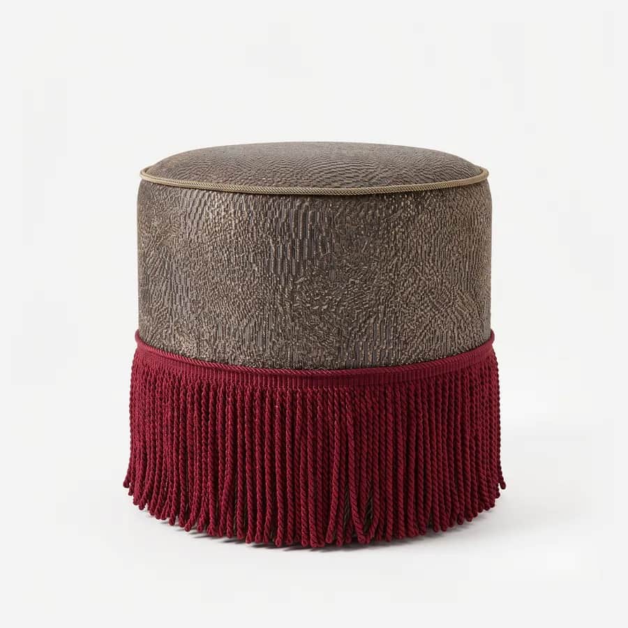 Kano Pouf pouf — round, fully upholstered pouf in a metallic pattern fabric, with a piped top edge and a deep twisted fringe skirt wra…