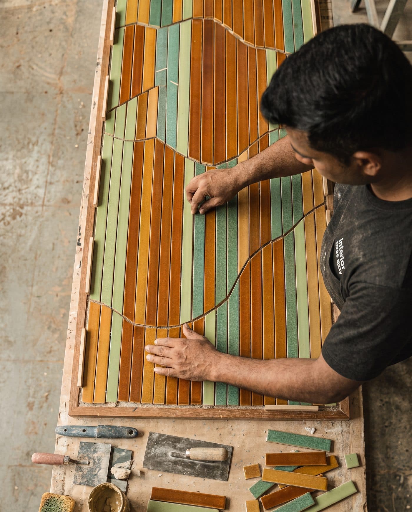 An Interior Three Sixty craftsman laying amber and green ceramic tiles into a wooden frame in the workshop